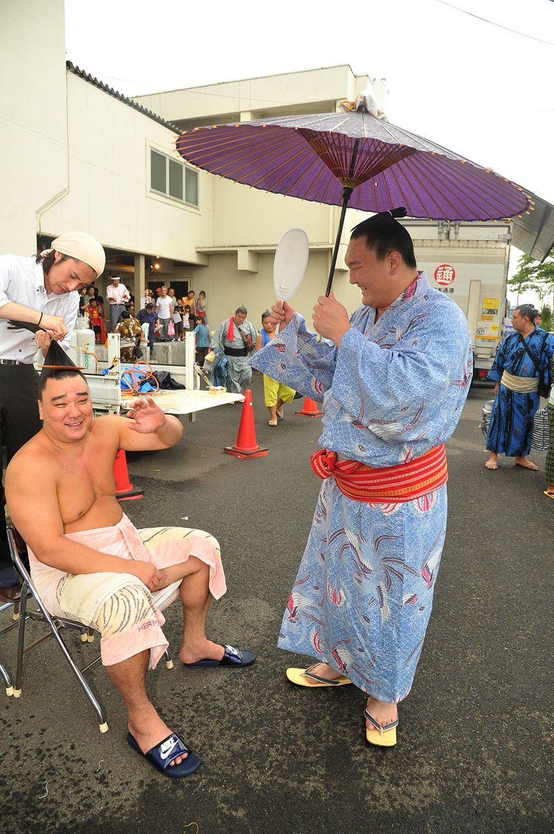 2014年8月11日＝宮城県加美町　取組後、日馬富士が屋外でマゲを直していると突然の雨。 帰り支度を終えた白鵬が傘を差しながら日馬富士をあおいだ。日馬富士は先輩の白鵬関にそんなことしてもらうなんて、「やめてくださいよ」と苦笑いを見せた。